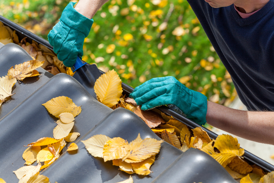 A man cleaning his gutters using a gutter scoop